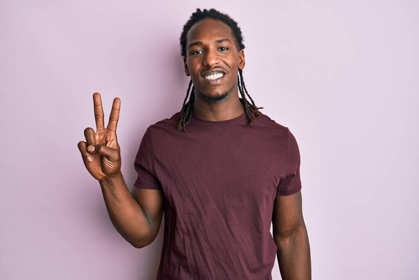 African american man with braids wearing casual clothes smiling with happy face winking at the camera doing victory sign. number two.  - Photo, Image