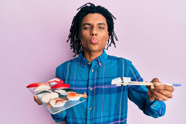 A fiatal afro-amerikai férfi szusit eszik evőpálcikával, miközben a kamerába néz, és egy csókot fúj, ami kedves és szexi. szerelem kifejezés.  - Fotó, kép