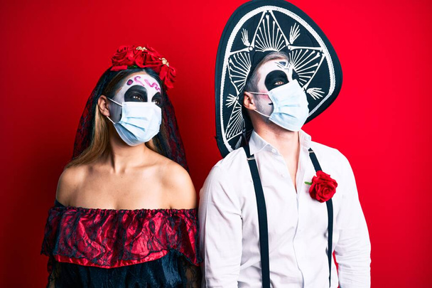Paar im Totenkostüm mit medizinischer Maske, mit einem Lächeln im Gesicht, natürlichem Gesichtsausdruck zur Seite blickend. Lachen selbstbewusst.  - Foto, Bild