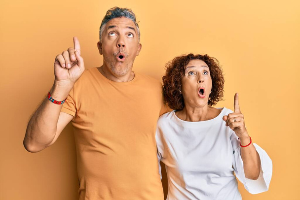Beautiful middle age couple together wearing casual clothes amazed and surprised looking up and pointing with fingers and raised arms.  - Photo, Image