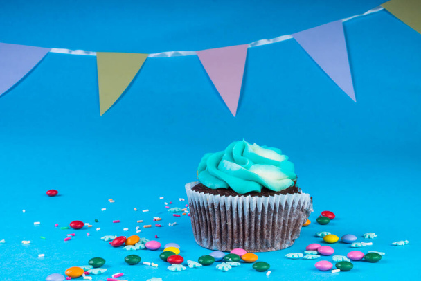 Cupcake al cioccolato con panna montata su sfondo blu, decorato con fiocchi di neve di zucchero, spruzzi, caramelle colorate, concetto di vacanza, biglietto di auguri - Foto, immagini