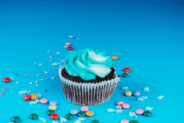 Suklaa Cupcake kermavaahtoa sinisellä pohjalla, koristeltu sokeri lumihiutaleet, strösselit, värikäs karkkeja, loma käsite, onnittelukortti - Valokuva, kuva