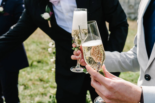The groom holds a glass of champagne on the background of the friends on nature at the wedding ceremony. Close up. Toast. - Foto, Bild