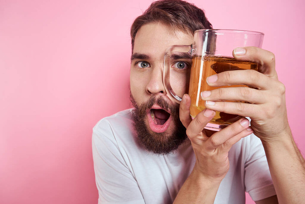 Hombre borracho con una taza grande de cerveza En un fondo rosa y una camiseta blanca vista relajada de una barba gruesa  - Foto, imagen