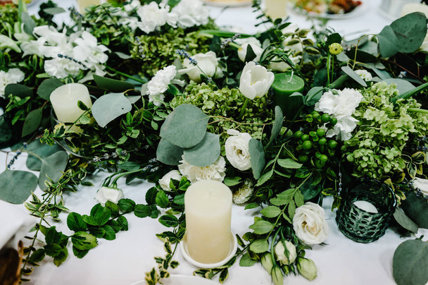 The composition of white flowers and greenery, candles standing on served table in the area of wedding party. Close up. - Valokuva, kuva