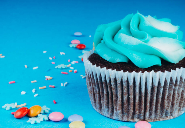 Suklaa Cupcake kermavaahtoa sinisellä pohjalla, koristeltu sokeri lumihiutaleet, strösselit, värikäs karkkeja, loma käsite, onnittelukortti - Valokuva, kuva