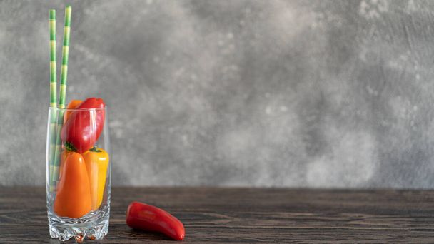 Sladký pepř uvnitř dlouhé sklenice na dřevěném stole. Červená oranžová a žlutá sladká paprika - Fotografie, Obrázek