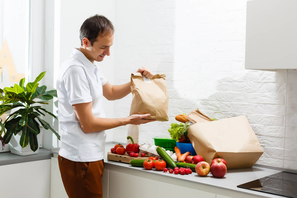 Egy férfi friss termékekkel az asztalnál, zárt térben, közelről. Élelmiszer-szállítási szolgáltatás - Fotó, kép