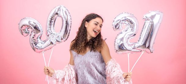 Festively dressed young girl laughing on a pink background with silver christmas balls in her hands horizontal - 写真・画像