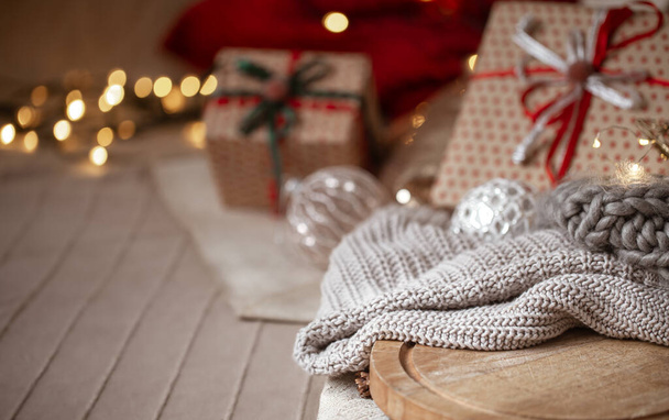 Рождественский фон с вязаным свитером в фокусе на размытом фоне рождественских украшений и завернутых подарков копировать пространство. - Фото, изображение