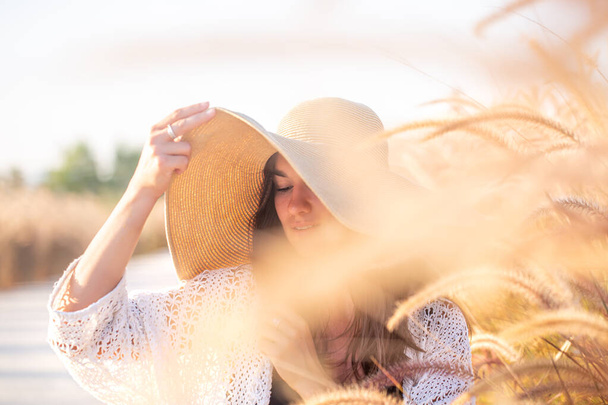 Retrato de uma jovem mulher ao sol, sentada em um campo, vestida com roupas de verão e um chapéu . - Foto, Imagem