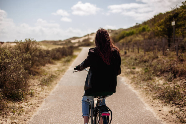 Achteraanzicht van een jong mooi meisje wandelt single op de fiets op de weg in zonnige dag tijd. - Foto, afbeelding