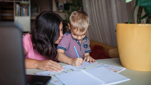 Vzdálené vzdělání. Evropská matka dělá online domácí úkoly se svým synem doma, společenská vzdálenost během karantény, vzdálená lekce, vnitřní rodinný životní styl - Fotografie, Obrázek