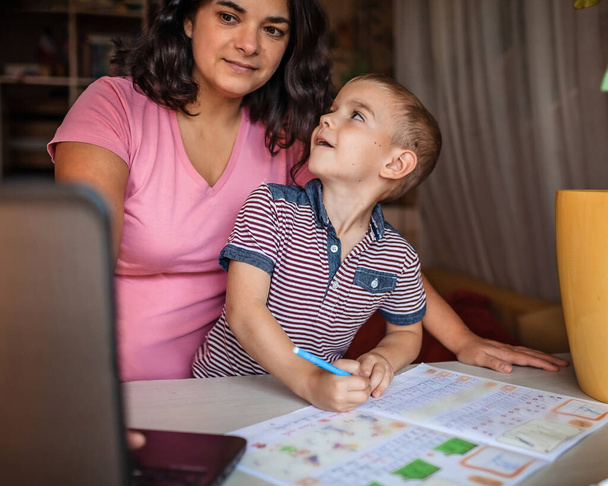Distanzierte Bildung. Europäische Mutter macht Online-Hausaufgaben mit ihrem kleinen Sohn zu Hause, soziale Distanz während der Quarantäne, Fernunterricht, Familienleben im Haus - Foto, Bild