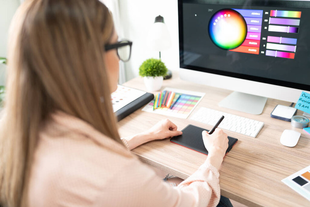 Вид спереду на жіночого графічного дизайнера, який використовує графічний планшет і вибирає правильний колір для дизайну в комп'ютері
 - Фото, зображення