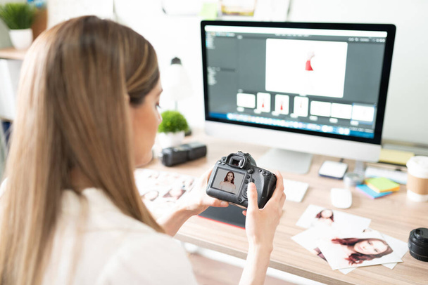 Vista trasera de una mujer sosteniendo una cámara delante de un ordenador y eligiendo fotos de una sesión de fotos reciente - Foto, imagen