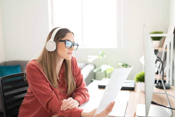 Pretty Caucasian brunetka czytanie niektórych dokumentów i pisanie treści podczas słuchania muzyki ze słuchawkami - Zdjęcie, obraz