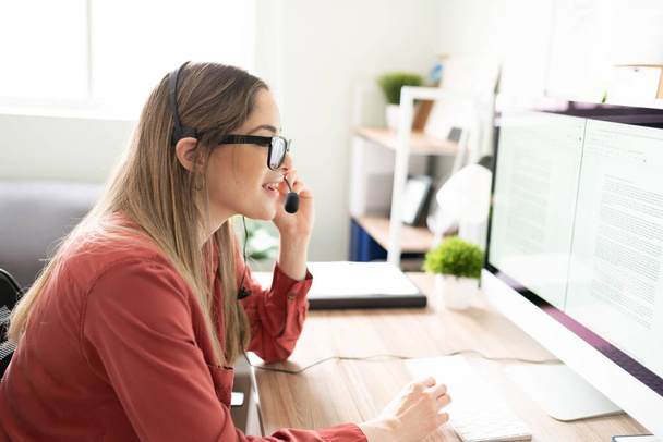 Visão de perfil de uma mulher trabalhando como intérprete enquanto olha para alguns documentos e usa um fone de ouvido em um escritório - Foto, Imagem