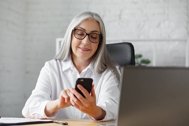 Senior grey-haired beautiful woman using smartphone and smiling. Happy businesswoman using mobile phone apps, texting message, browsing internet, shopping online. Mature people with mobile devices - 写真・画像