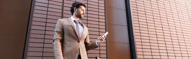 bearded businessman looking at smartphone near building, banner - 写真・画像