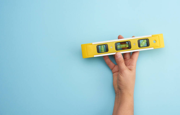 uchwyt ręczny żeński plastikowy żółty poziom narzędzia z kapsułek na niebieskim tle, przestrzeń kopiowania - Zdjęcie, obraz