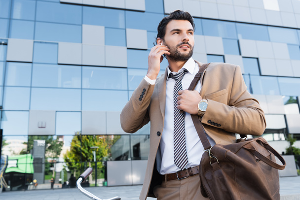 bearded businessman adjusting wireless earphones while standing near building  - Fotó, kép