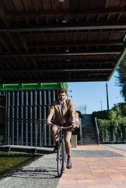 full length of businessman in wireless earphones riding bicycle  - Fotoğraf, Görsel