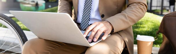 partial view of businessman using laptop near paper cup, banner  - Foto, Bild