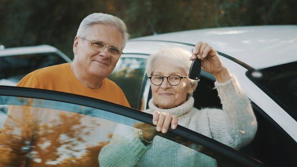 Το ηλικιωμένο ζευγάρι αγόρασε καινούριο αυτοκίνητο. Στέκεται κοντά στην πόρτα και γυναίκα κρατώντας τα κλειδιά - Φωτογραφία, εικόνα