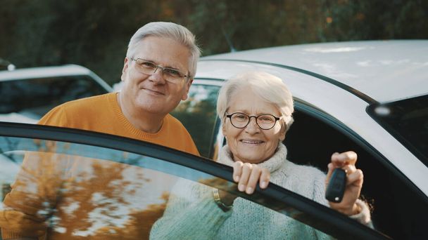 Старшая пара купила новую машину. Стоя рядом с дверью, женщина держит ключи - Фото, изображение