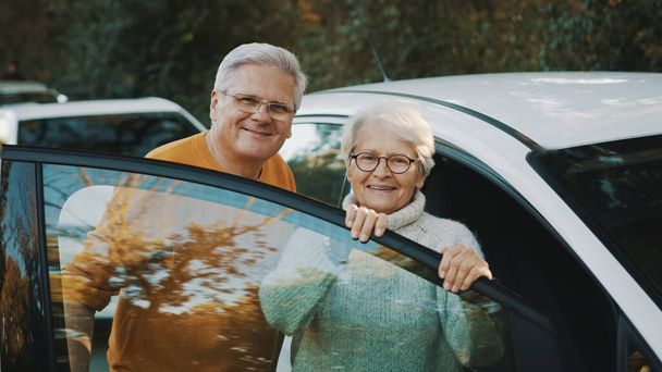 Una pareja de ancianos compró un auto nuevo. De pie cerca de la puerta y la mujer sosteniendo llaves - Foto, Imagen