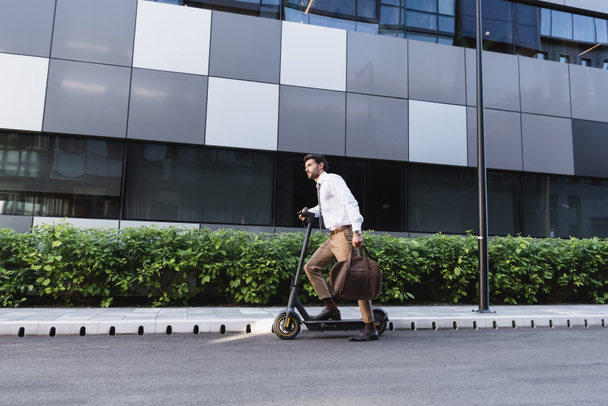 bearded businessman in formal wear riding electric scooter and holding bag - Photo, Image