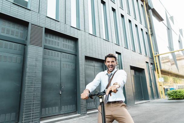 amazed businessman in suit riding electric scooter near building  - Φωτογραφία, εικόνα