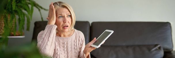 femme mature triste et déprimée assise sur le canapé et utilisant une tablette numérique - Photo, image