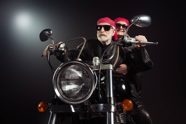 Photo of two cool old bikers white hair man lady couple drive vintage chopper traveling together feel young wear rocker leather jacket outfit red bandana isolated black color background - 写真・画像
