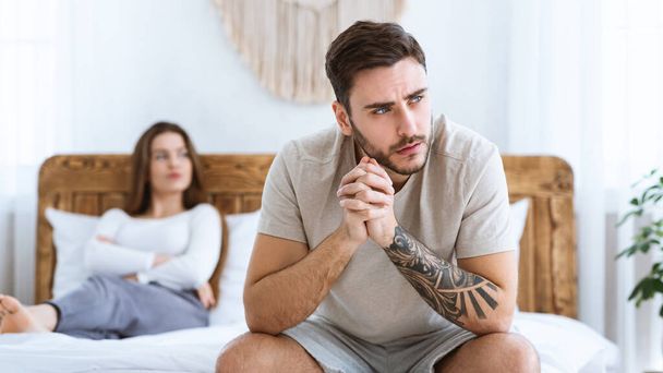 Man and woman feeling stressed and angry at each other, sits on wooden bed and look to side of free space - Фото, изображение