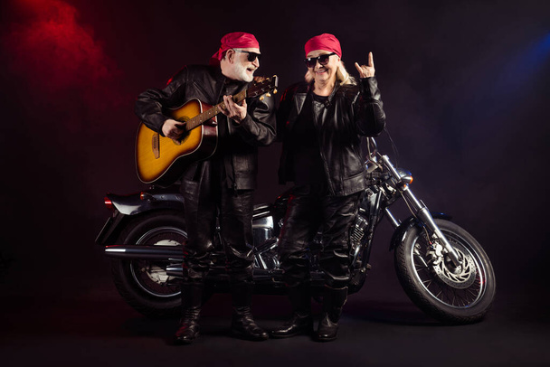 Photo of aged cool bikers man lady couple chopper moto feel young rock bike festival meeting play sing guitar show horns wear trendy rocker leather outfit isolated black color background - Foto, afbeelding