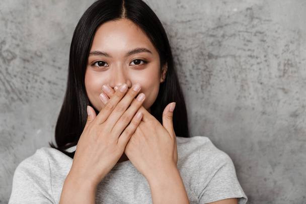 Image of joyful beautiful asian girl covering her mouth while posing indoors - Fotoğraf, Görsel