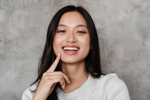 Imagen de alegre hermosa chica asiática sonriendo y mirando a la cámara mientras posan en el interior - Foto, imagen