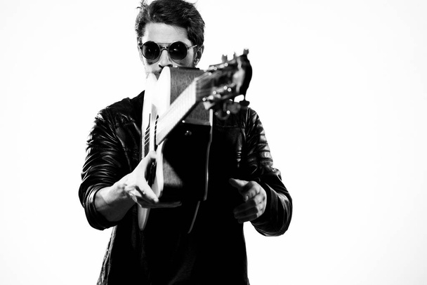 A man plays the guitar in a black leather jacket with sunglasses on a light background - Photo, Image