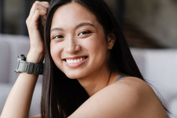 Image of beautiful asian girl in smartwatch smiling and looking at camera indoors - Zdjęcie, obraz