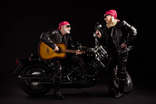 Foto de duas pessoas de idade motociclistas homem senhora dueto helicóptero moto rock festival reunião tocar guitarra cantar canções juventude anos popular grupo desgaste balancim jaqueta de couro isolado preto cor fundo - Foto, Imagem