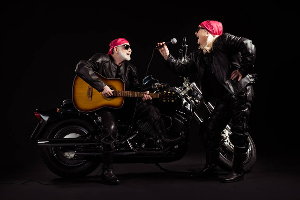 Full body photo of aged bikers man lady duet couple chopper moto rock festival meeting play guitar sing songs youth years group wear rocker leather jacket isolated black color background - 写真・画像
