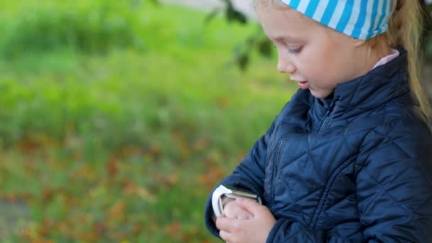 Lapsi käyttää älykelloa ulkona syyspuistossa. Poika puhuu videopuhelussa älypuhelimella. Koulutyttö käyttää kosketusnäytön näyttö kellot selaamassa internetissä. Älykkäät lapset rannekello GPS tracker. - Materiaali, video