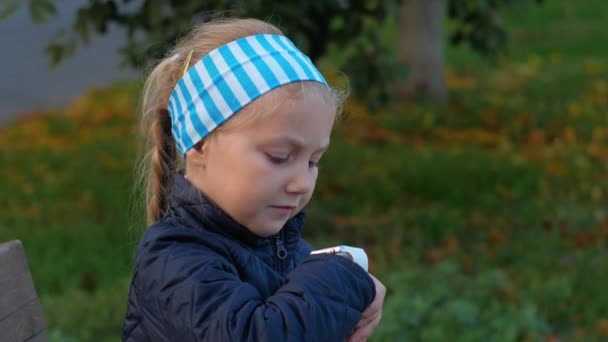 Dziecko korzystające ze smartwatch outdoor w jesiennym parku. Dzieciak gadający na vdeo przez smartfona. Uczennica za pomocą ekranu dotykowego wyświetlacza na zegarkach przeglądających internet. Inteligentny zegarek dla dzieci z nadajnikiem GPS. - Materiał filmowy, wideo