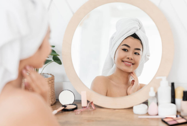 Sorrindo asiático mulher envolto em toalha olhando para espelho - Foto, Imagem
