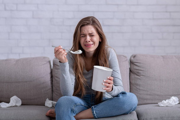 Emocjonalne jedzenie. zestresowana kobieta płacze na kanapie z wiadrem lodów, ogląda smutny film i czuje się przygnębiona - Zdjęcie, obraz