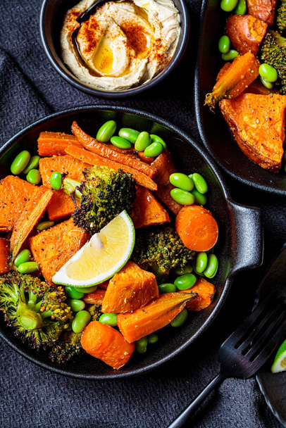 Baked vegetables in cast iron pans, dark background. Baked sweet potatoes, broccoli, carrots, and beans. - Φωτογραφία, εικόνα