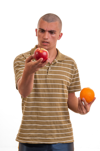 young man comparing apples to oranges - Фото, изображение