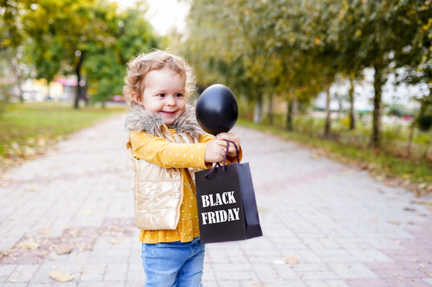 happy child holding shopping bag on black friday and black inflatable ball standing in the park - Fotó, kép